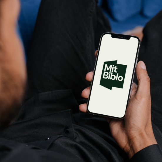 Hånd, der holder en telefon, hvor logoet til Mit Biblo-appen ses