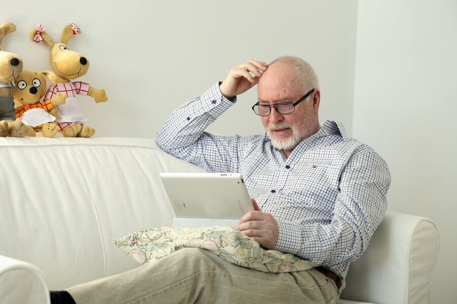 Foto af ældre herre, der læser på en tablet i en sofa