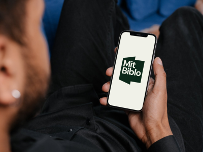 Hånd, der holder en telefon, hvor logoet til Mit Biblo-appen ses
