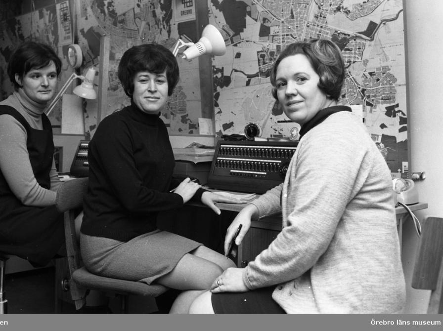 Växeltelefonister 31 januari 1969. Tre kvinnor som arbetar i en telefonväxel. På väggen hänger det kartor på Örebro kommun. En kvinna har klänning och polotröja på sig. Kvinnan som sitter i mitten har kjol och polotröja på sig. ved Örebro Kuriren - Örebro County Museum, Sweden - CC BY-NC. https://www.europeana.eu/item/916121/S_OLM_photo_OLM_2012_8_11096